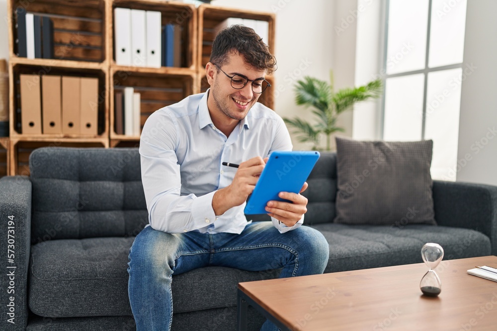 Young hispanic man psychologist smiling confident using touchpad at psychology clinic Young hispanic man psychologist smiling confident using touchpad at psychology clinic
