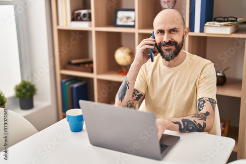 Young bald man using laptop talking on smartphone at home © Krakenimages.com