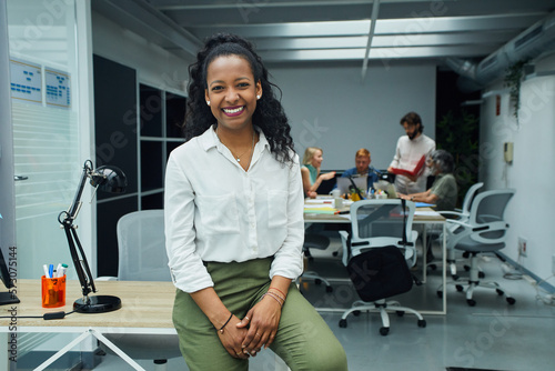 Fotografi Portrait of smiling young African American professional female sitting at modern office desk