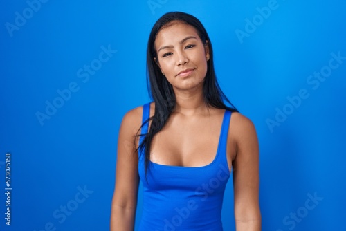 Hispanic woman standing over blue background relaxed with serious expression on face. simple and natural looking at the camera.