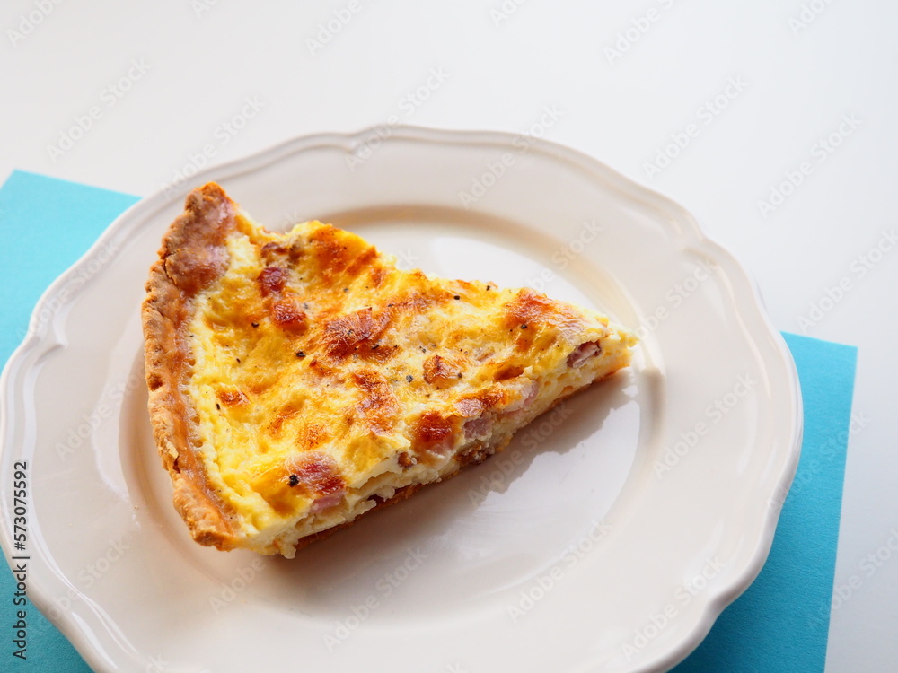 Homemade traditional french Quiche Lorraine, real recipe, slice on a plate, white and blue background, space for text