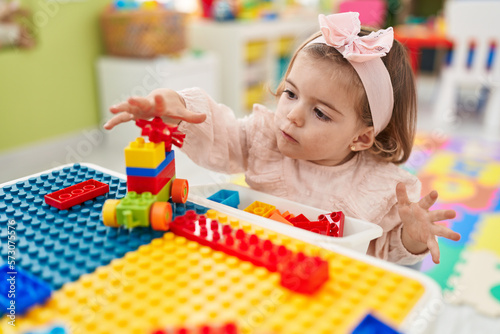 Adorable blonde toddler playing with construction blocks sitting on table at kindergarten