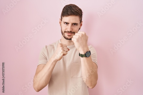 Hispanic man with beard standing over pink background ready to fight with fist defense gesture, angry and upset face, afraid of problem