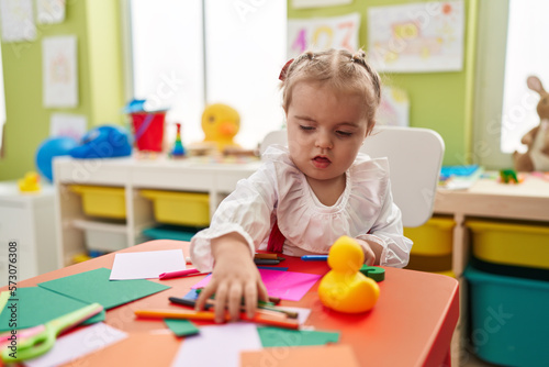Adorable blonde toddler preschool student sitting on table drawing on paper at kindergarten