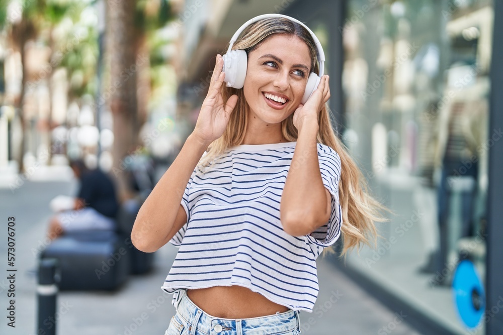 Young blonde woman listening to music at street