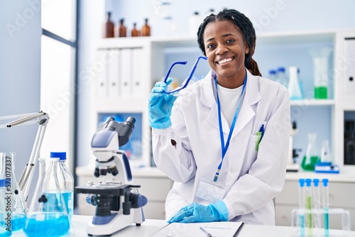 African american woman scientist smiling confident holding security glasses at laboratory