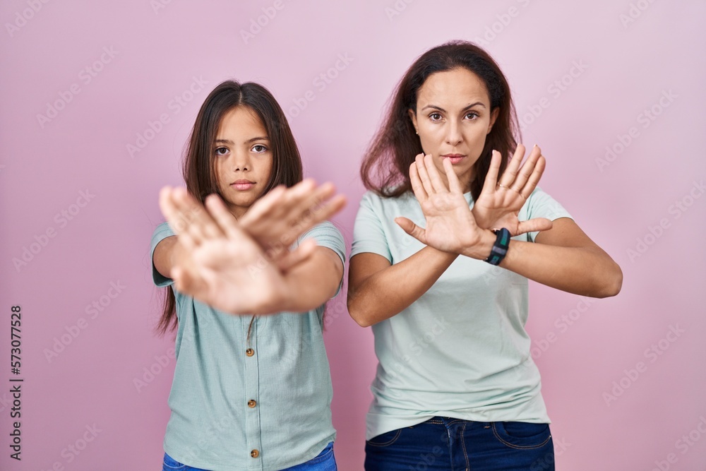 Young mother and daughter standing over pink background rejection expression crossing arms and palms doing negative sign, angry face Young mother and daughter standing over pink background rejection expression crossing arms and palms doing negative sign, angry face