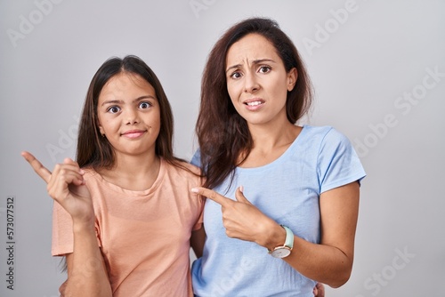 Young mother and daughter standing over white background pointing aside worried and nervous with forefinger  concerned and surprised expression