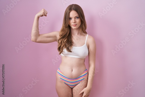 Caucasian woman wearing lingerie over pink background strong person showing arm muscle, confident and proud of power © Krakenimages.com