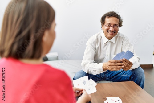 Middle age man and woman couple smiling confident playing poker cards at home
