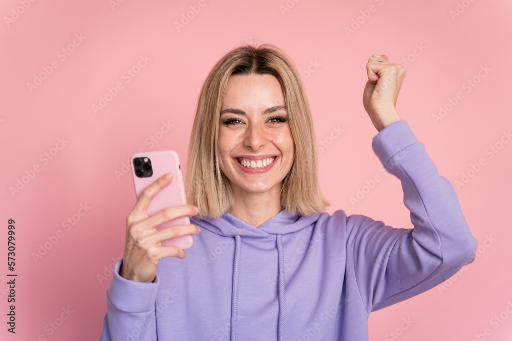 Fototapeta premium Excited woman with smartphone on pink background in studio