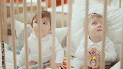 Two adorable babies holding toy sitting on cradle at bedroom