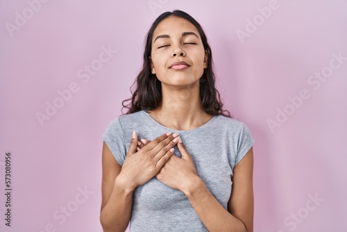 Young brazilian woman wearing casual t shirt over pink background smiling with hands on chest with closed eyes and grateful gesture on face. health concept. © Krakenimages.com