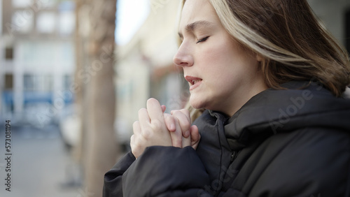 Young blonde woman praying with closed eyes at street