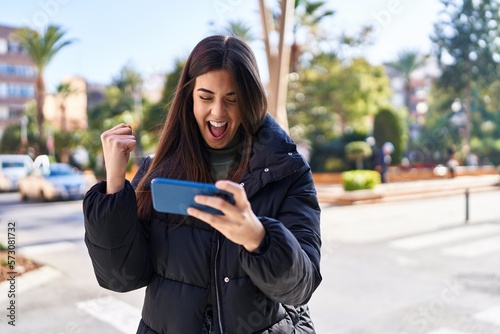 Young beautiful hispanic woman smiling confident playing video game at street photo