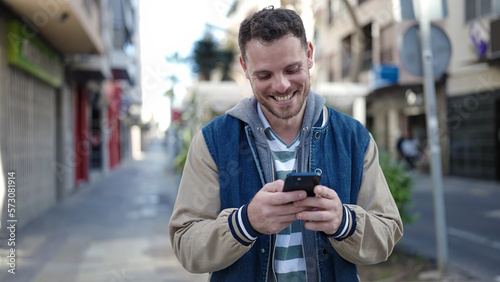 Young caucasian man smiling using smartphone at street