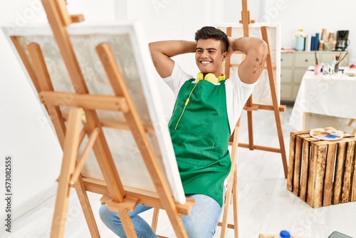 Young hispanic man smiling confident relaxed with hands on head at art studio