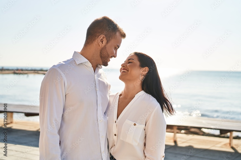 Man and woman couple smiling happy hugging each other standing at seaside