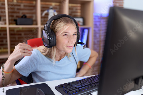 Young caucasian woman playing video games wearing headphones suffering of backache, touching back with hand, muscular pain