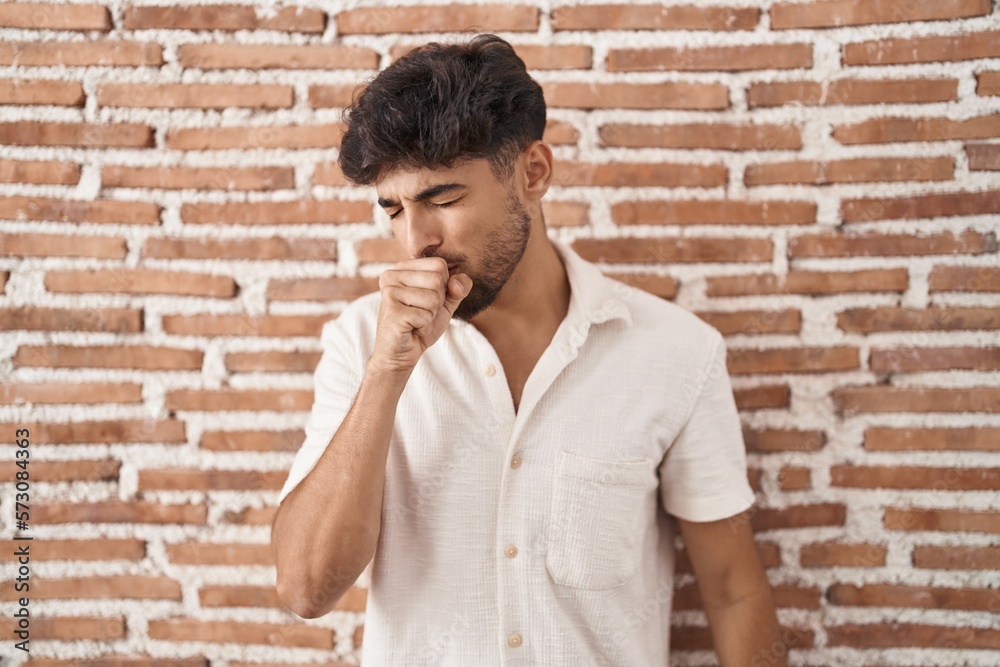 Arab man with beard standing over bricks wall background feeling unwell and coughing as symptom for cold or bronchitis. health care concept.