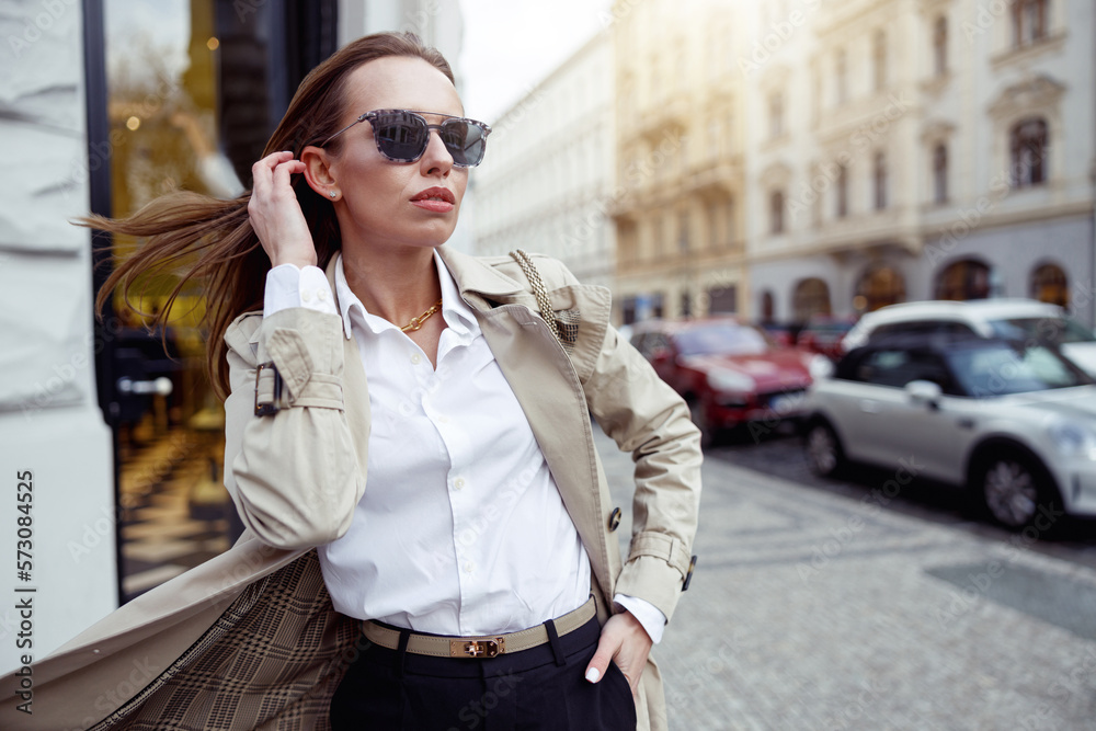 Fototapeta premium Stylish woman in coat standing on city street background and looking at side. High quality photo