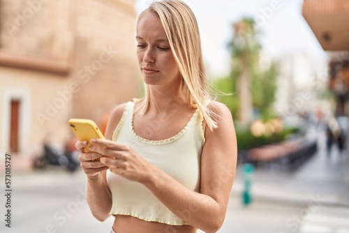 Young blonde woman using smartphone with relaxed expression at street