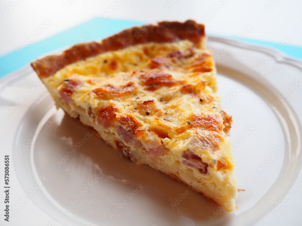 Homemade traditional french Quiche Lorraine, real recipe, slice on a plate, closeup, white and blue background Homemade traditional french Quiche Lorraine, real recipe, slice on a plate, closeup, white and blue background