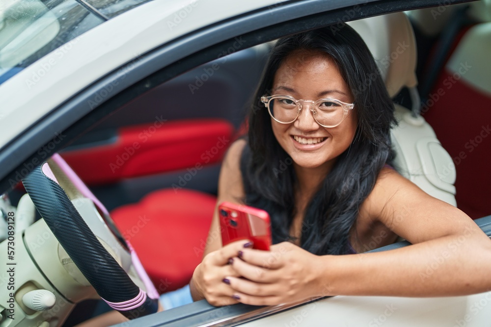 Young chinese woman using smartphone sitting on car at street