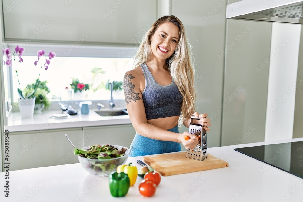 Young woman smiling confident scratching carrot for salad at kitchen