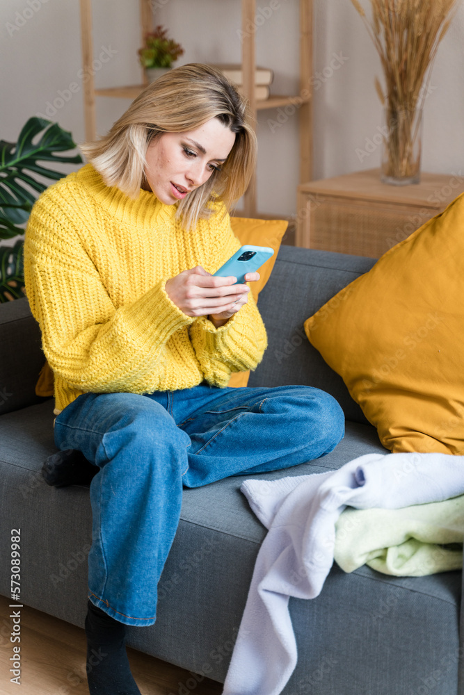Obraz premium Young woman using smartphone on sofa taking pictures of her clothes