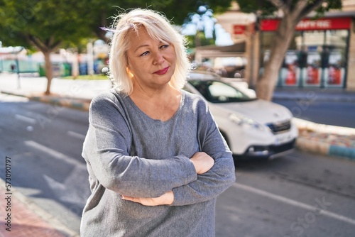 Middle age blonde woman standing relaxed with arms crossed gesture at street