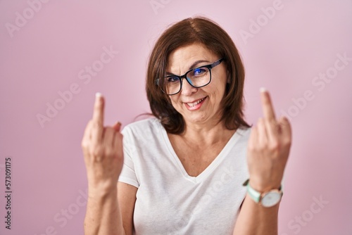 Middle age hispanic woman standing over pink background showing middle finger doing fuck you bad expression  provocation and rude attitude. screaming excited