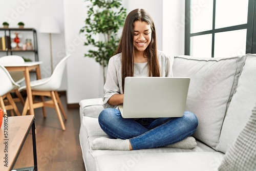 Young latin woman using laptop sitting on sofa at home
