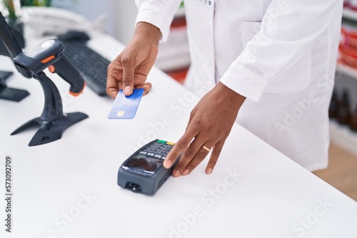 Middle age african american woman pharmacist using credit card and data phone at pharmacy