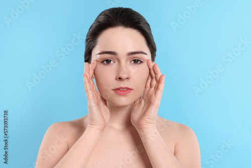 Young woman massaging her face on turquoise background