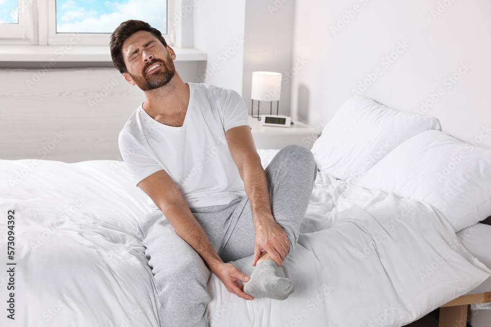 Man suffering from leg pain on bed at home Man suffering from leg pain on bed at home