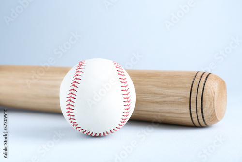 Wooden baseball bat and ball on light grey background, closeup. Sports equipment