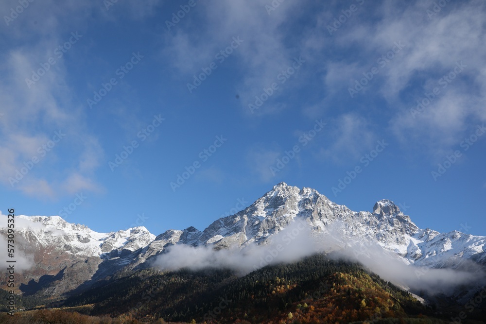 Picturesque landscape of high mountains covered with thick mist under blue sky on autumn day
