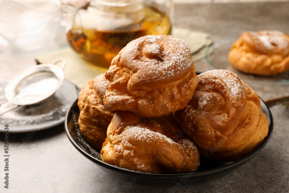 Delicious profiteroles with powdered sugar in bowl on grey table Delicious profiteroles with powdered sugar in bowl on grey table