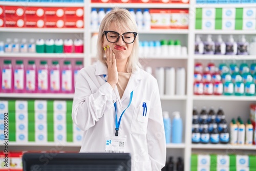 Young caucasian woman working at pharmacy drugstore touching mouth with hand with painful expression because of toothache or dental illness on teeth. dentist