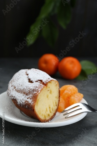 Piece of delicious homemade yogurt cake with powdered sugar and tangerines on gray table