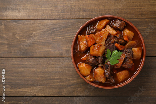 Delicious beef stew with carrots, parsley and potatoes on wooden table, top view. Space for text