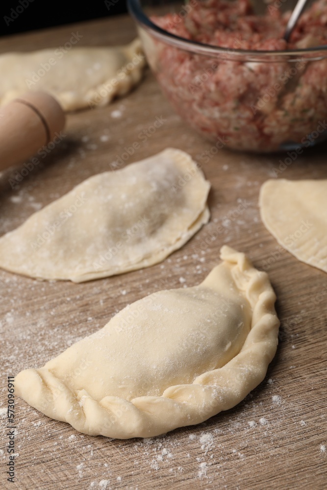 Uncooked chebureki, minced meat and rolling pin on wooden table Uncooked chebureki, minced meat and rolling pin on wooden table