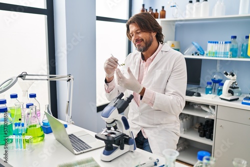 Middle age man scientist holding herb with tweezers at laboratory