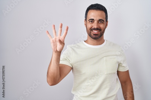 Hispanic man with beard standing over isolated background showing and pointing up with fingers number four while smiling confident and happy.