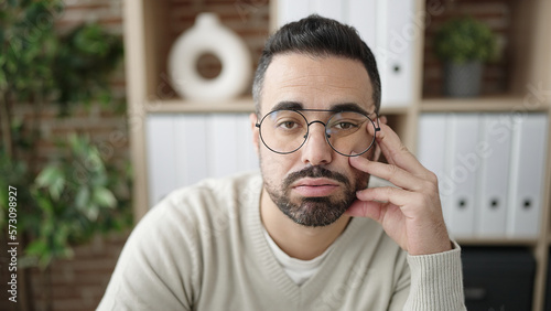 Young hispanic man sitting on sofa with tired expression at office