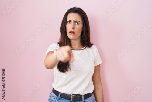 Young brunette woman standing over pink background pointing displeased and frustrated to the camera  angry and furious with you