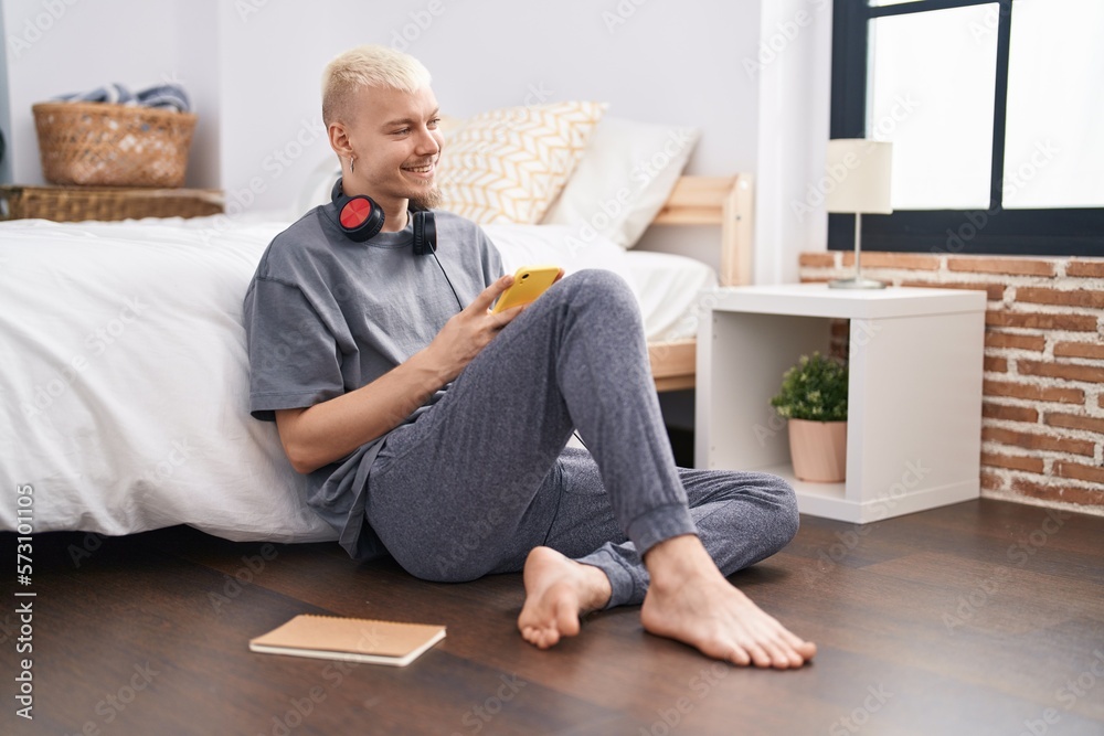 Young caucasian man using smartphone sitting on floor at bedroom