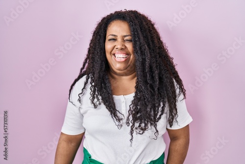 Plus size hispanic woman standing over pink background winking looking at the camera with sexy expression  cheerful and happy face.