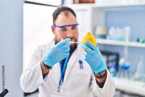 Young hispanic man scientist injecting on lemon at laboratory